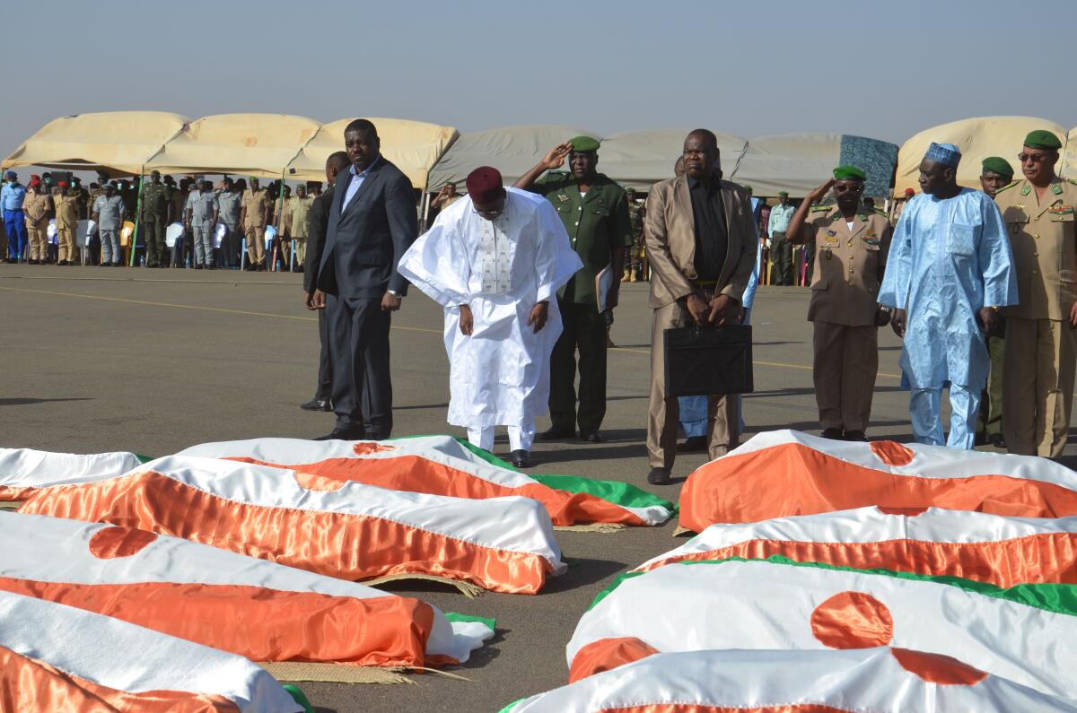 Niger President Mahamadou Issoufou bows near the bodies of military personnel at the Niamey air base on Friday. Niger's government has declared three days of mourning following an attack at a military base.
