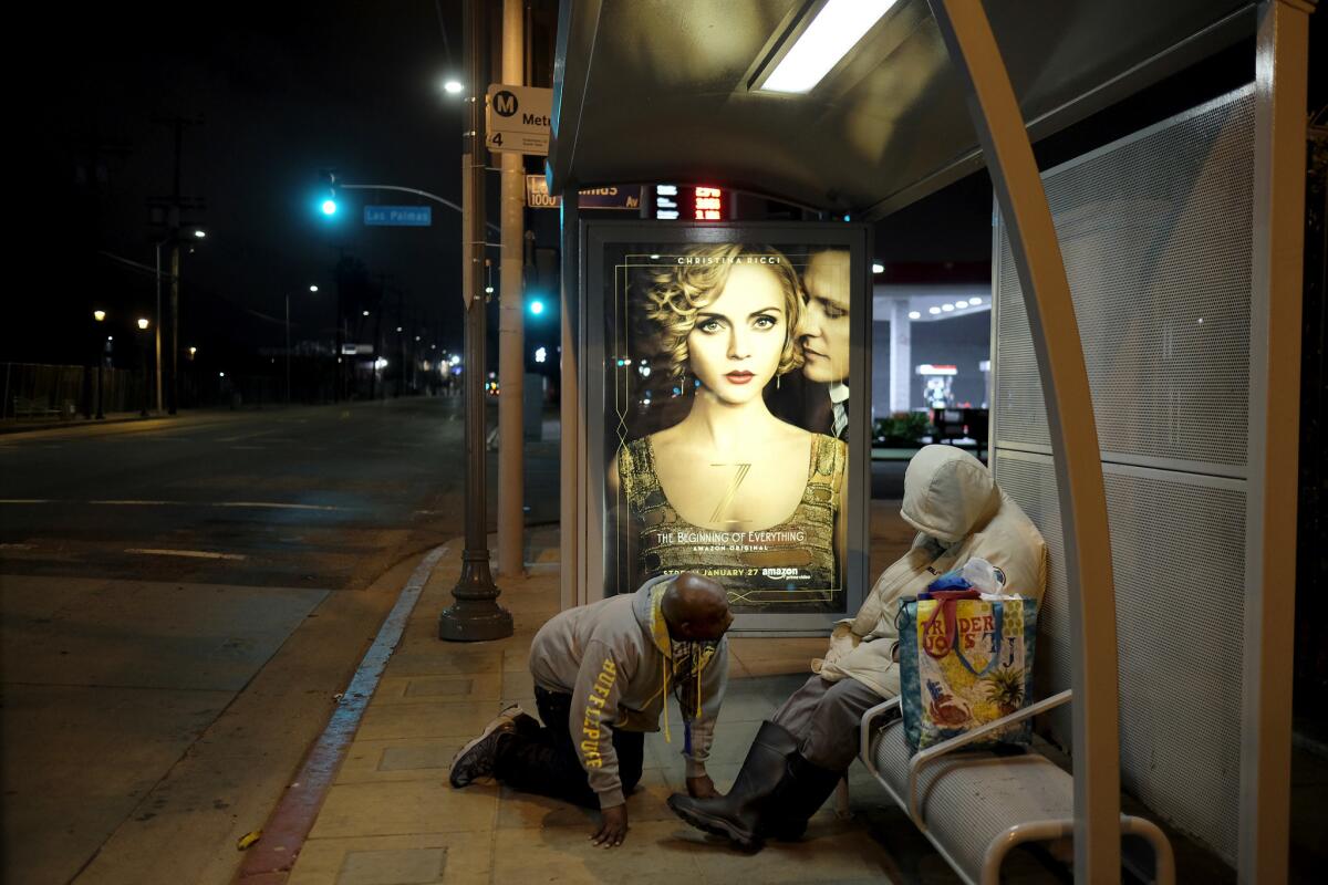 Housing Works caseworker Anthony Ruffin kneels to check on a homeless woman sleeping on a bus bench in Hollywood.