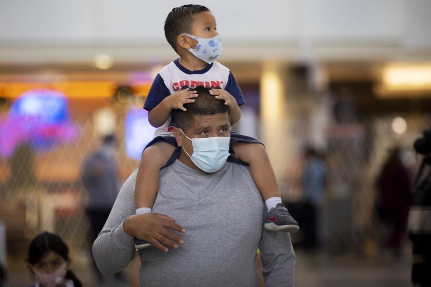 LOS ANGELES, CA - NOVEMBER 17: During the global coronavirus Mario Tejada walks with his son Mario Tejada, Jr. age 3, on his shoulders both wearing masks in Tom Bradley international at LAX on Tuesday, Nov. 17, 2020 in Los Angeles, CA. Los Angeles International Airport will begin issuing molecular or PCR tests in two terminals this week and has plans to quickly expand the program in order to help detect coronavirus and slow its spread. (Francine Orr / Los Angeles )