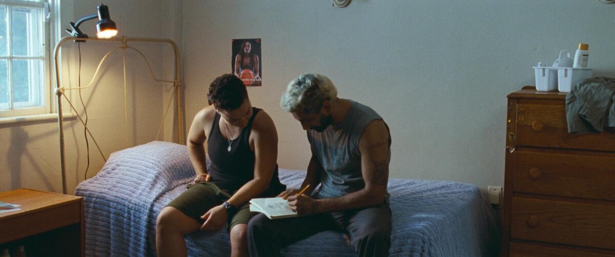 Chelsea Lee and Riz Ahmed looking at a sketchbook while sitting on a bed in "Sound of Metal"