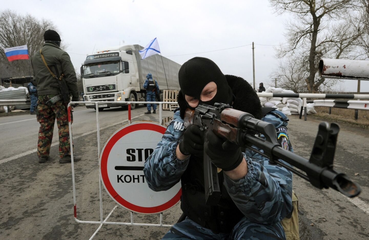 One of the armed masked men who call themselves members of Ukraine's disbanded elite Berkut riot police force aims his Klashnikov rifle at a checkpoint under Russian flags on a highway that connects the Black Sea Crimea peninsula to mainland Ukraine.