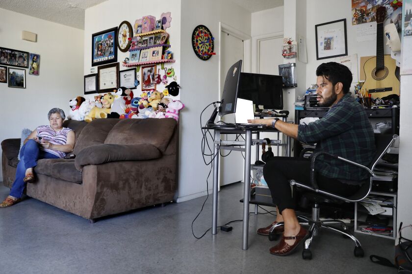 SANTA ANA, CALIFORNIA: Jonatan Gutierrez, 32, right, works from home as his mom Rocio Urzua, 54, at left, relaxes before going to work later that afternoon, at home in Santa Ana, California on Friday, July 2, 2021. Medi-Cal expansion will offer relier to income eligible adults 50 and older regardless of immigration status. (Christina House / Los Angeles Times)