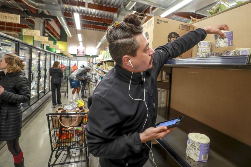 Jaeci King, who said he's been to several stores looking for toilet paper, picks up a roll of toilet paper while calling a friend to see if they want some at Jimbo's in Carmel Valley on Friday, March 13, 2020 in San Diego, California.