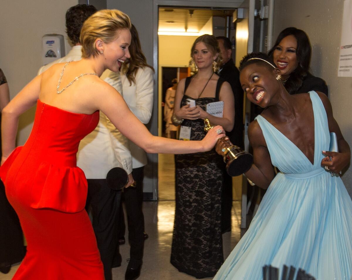 Actresses Jennifer Lawrence, left, and Lupita Nyong'o playfully fight over the Oscar Nyong'o won for actress in a supporting role. Both were examples of the evening's easy hair, easy makeup trend.