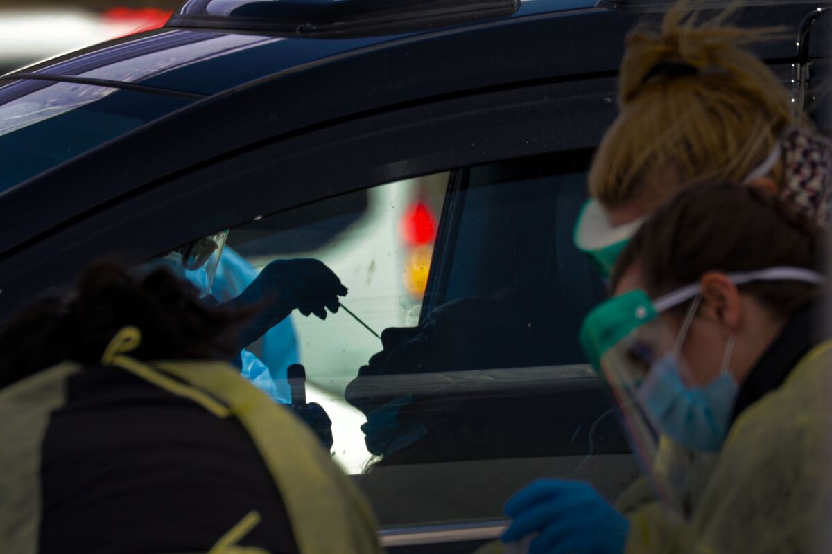 A San Bernardino County healthcare worker takes a sample at a drive-through test collection event at the county fairgrounds in Victorville.