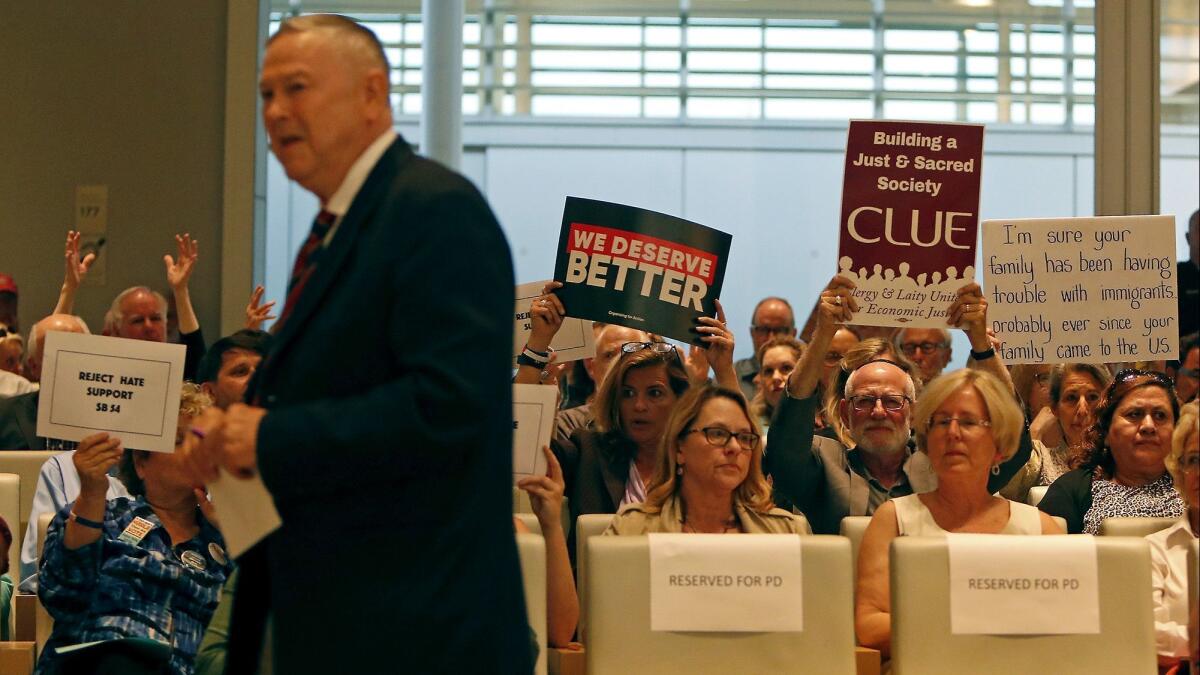 Supporters of Senate Bill 54, a California "sanctuary state" law, hold up signs after U.S. Rep. Dana Rohrabacher (R-Cosa Mesa), left, spoke against it during Tuesday's Newport Beach City Council meeting.