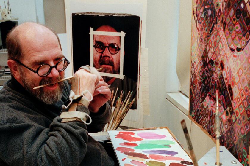 FILE - In this Jan. 3, 1996, file photo, Chuck Close, 55, using a hand brace to hold his paint brush, adjusts the brush with his teeth while working in his New York studio. Since suffering a partial paralysis in 1988 due to a spinal artery collapse, Close does not have the strength to grip the brush. Close who is best known for his monumental grid portraits and photo-based paintings of family and famous friends, has died on Thursday, Aug. 19, 2021, at age 81. (AP Photo/Mark Lennihan, File)