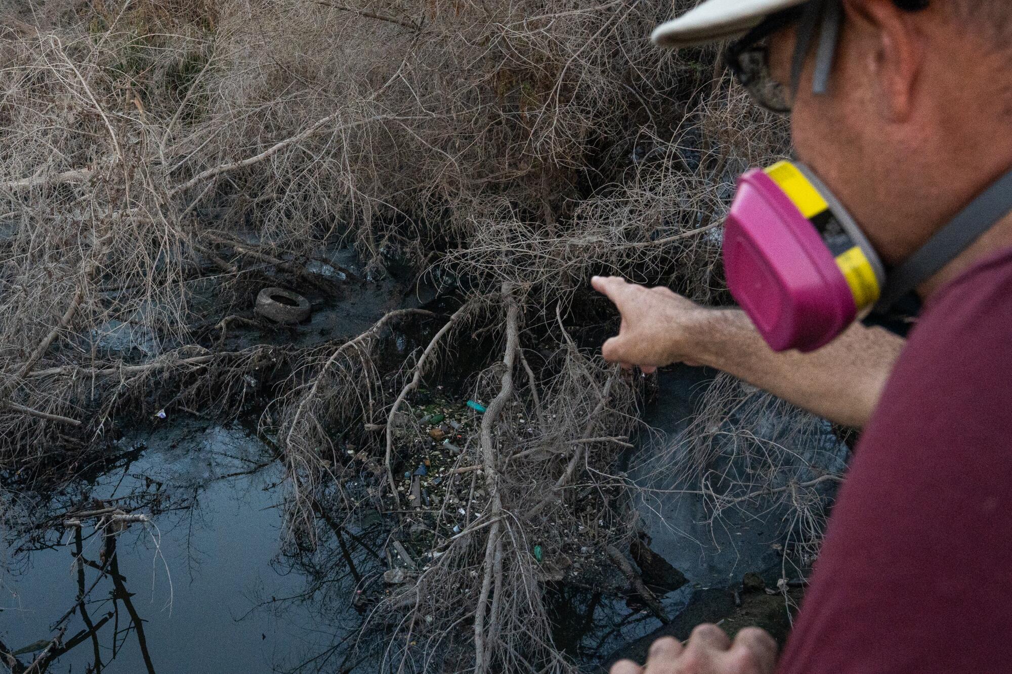 Ángel Granados points at the pollution in the Tijuana River under Hollister Street.