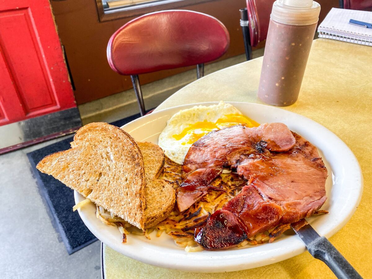 A plate with ham, eggs, toast and a squeeze bottle of sauce on a diner table