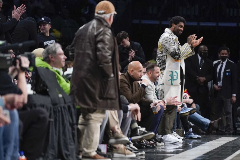 Kyrie Irving applauds his Nets teammates while standing near his front row seat.