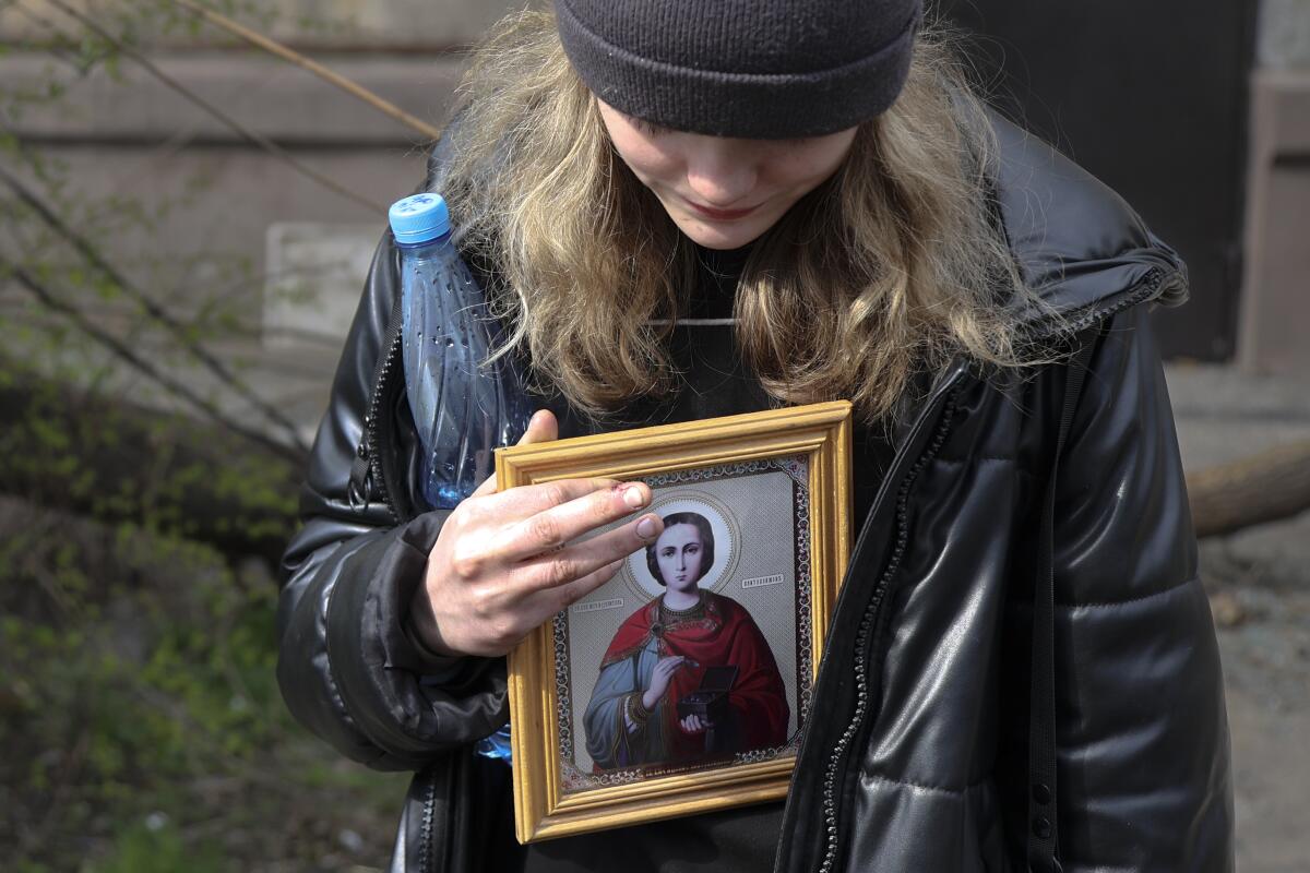 A woman holds a water bottle and a framed religious icon.