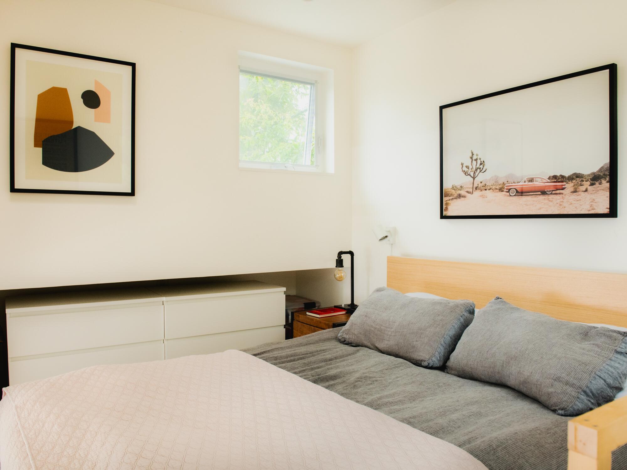 A bedroom with art on the walls and a small square window.