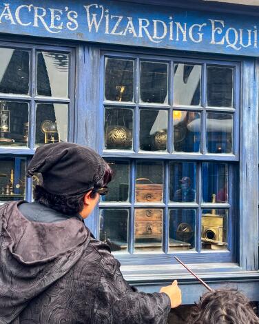 Guests waving a wand outside a shop window in Wizarding World. 