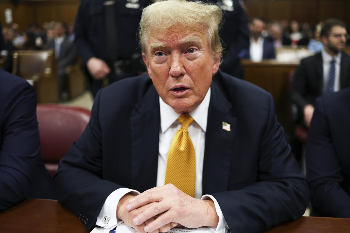 Former President Trump sits in court wearing a yellowish tie.