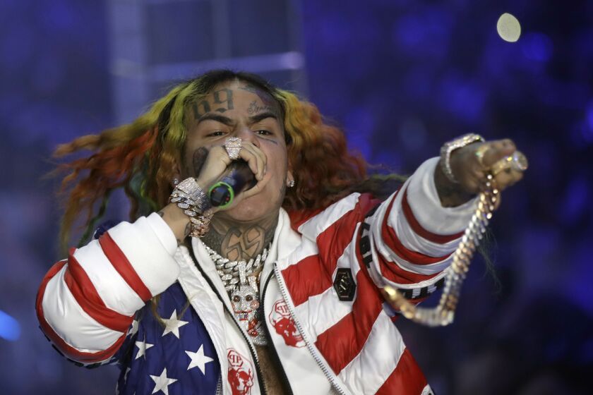 Tekashi 6ix9ine performing on stage holding a mic and wearing a jacket that looks like the American flag