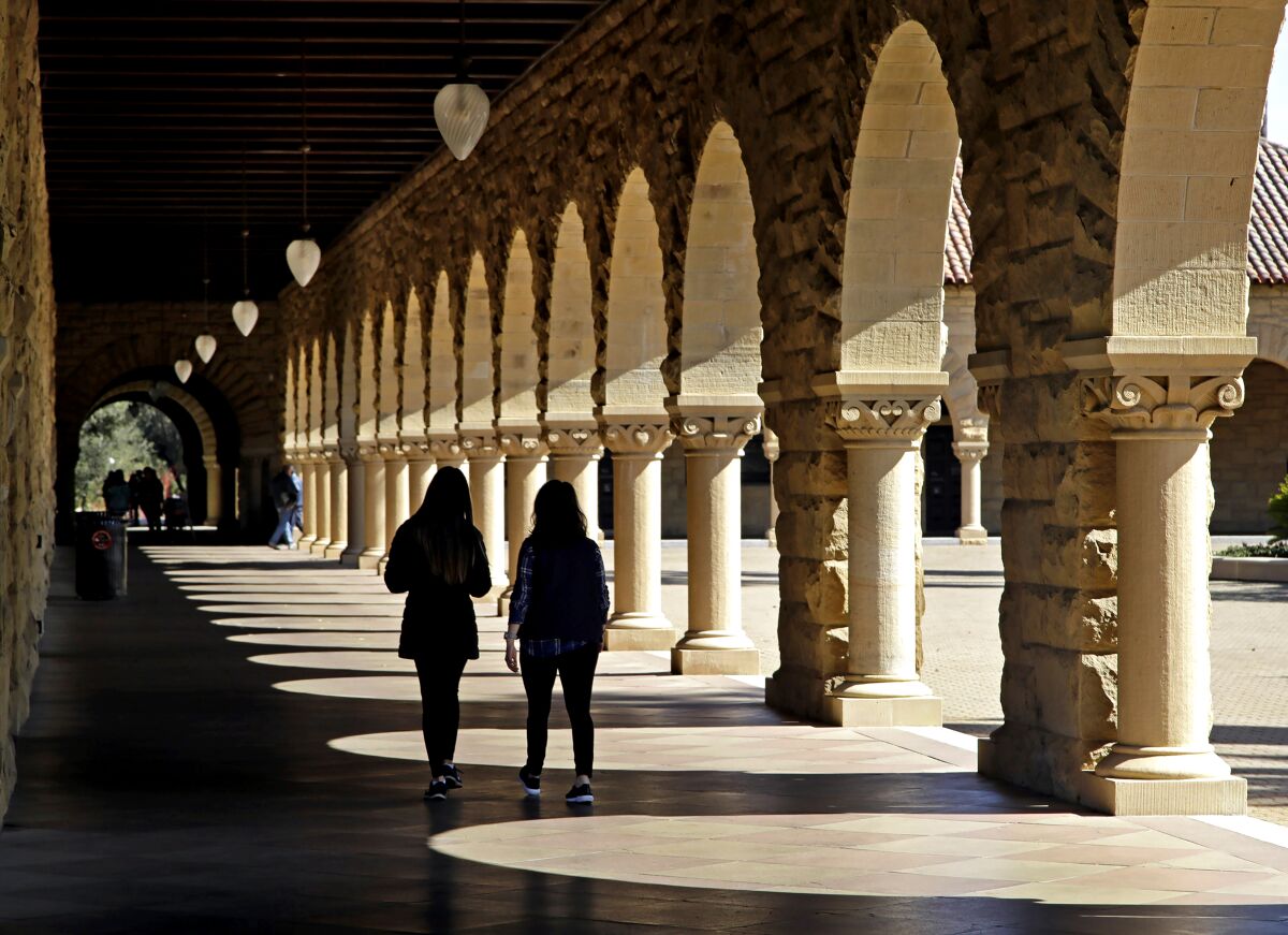 Students walk next to arches on a college campus.
