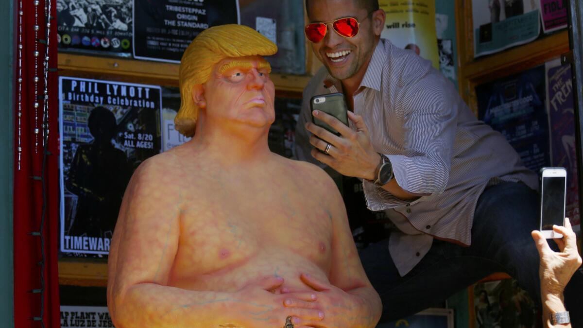 Jason Burch, 38, right, of West Hollywood, takes a selfie with a nude statue of Donald Trump at the entrance of Soap Plant Wacko in Los Angeles.