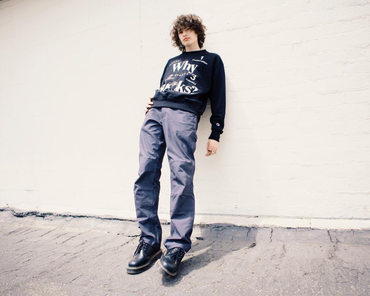 A tall teenage boy stands in front of a white concrete wall