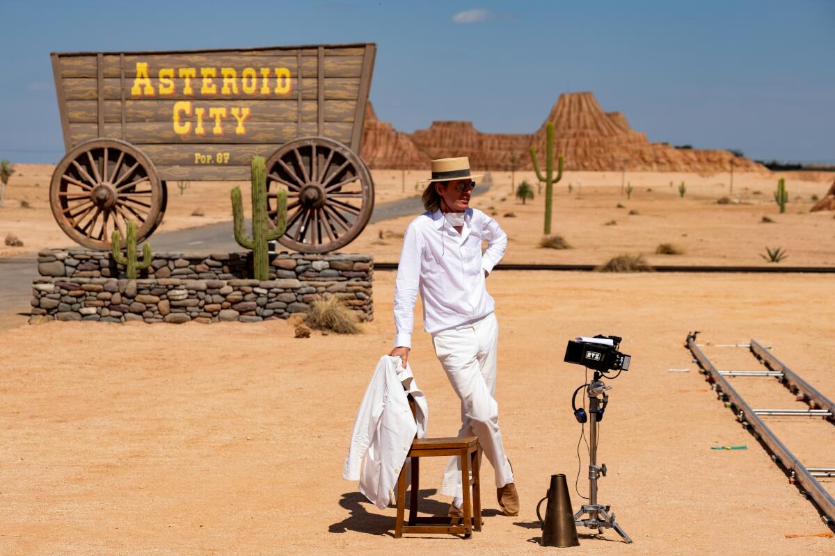 Wes Anderson dressed all in white and wearing a skimmer, leans on a chair on the desert set of "Asteroid City."