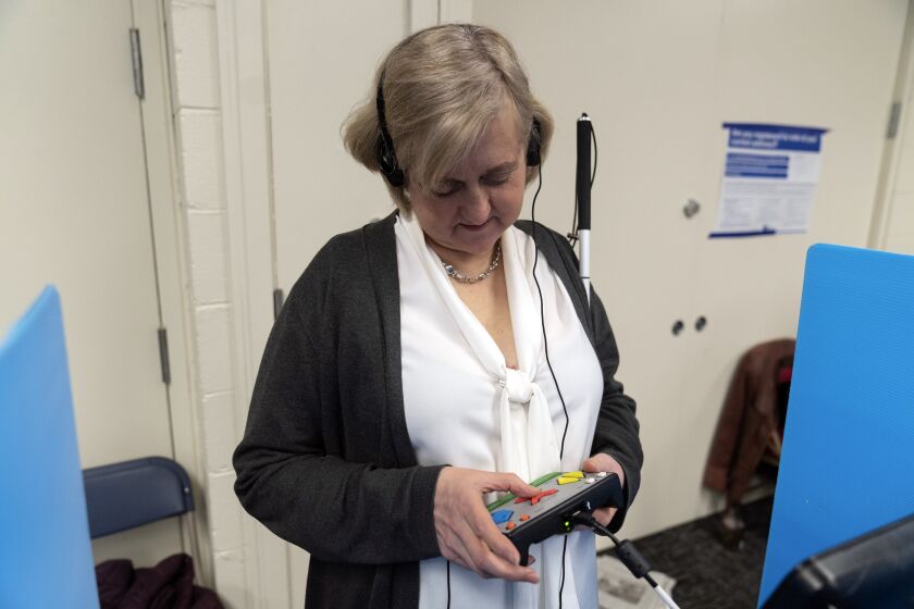 Patti Chang, who is blind, uses headphones and audio along with an electronic controller outfitted with braille to vote in the Chicago mayoral runoff election at the Roden Branch of the Chicago Public Library Wednesday, March 22, 2023, in Chicago. Like many voters with disabilities, Chang faces barriers at the polls most voters never even consider — missing ramps or door knobs, for example. The lack of help or empathy from some poll workers just adds to the burden for people with disabilities. (AP Photo Erin Hooley)
