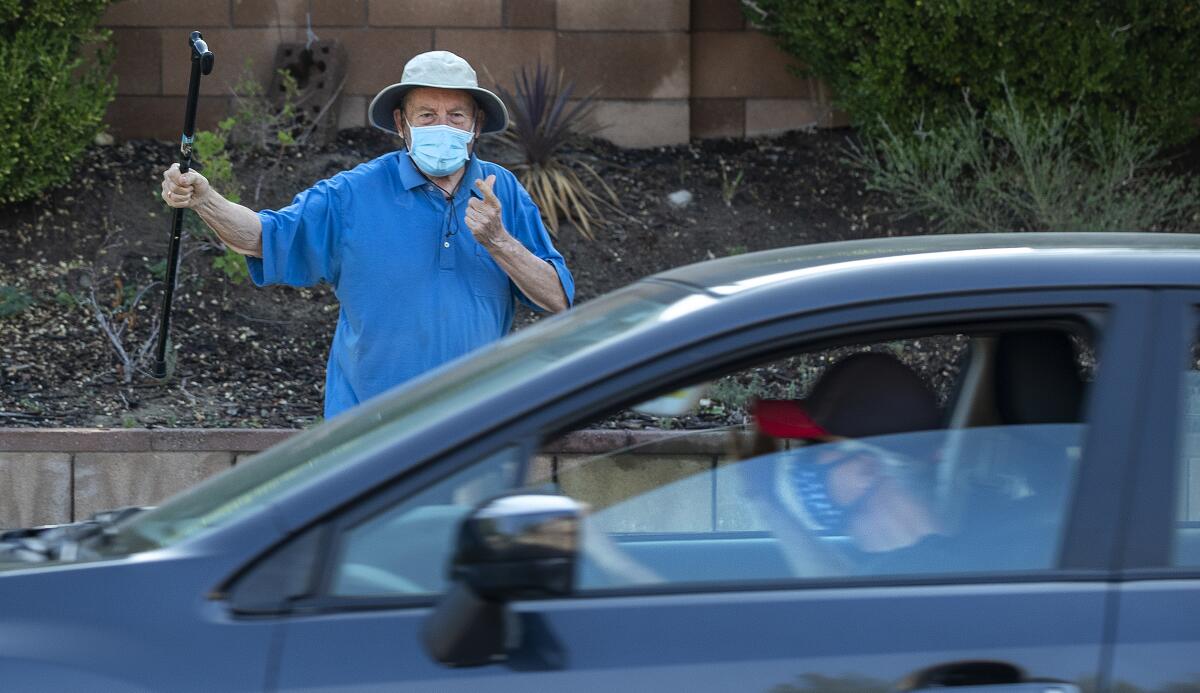 A man wearing a mask and holding a cane talks to a driver