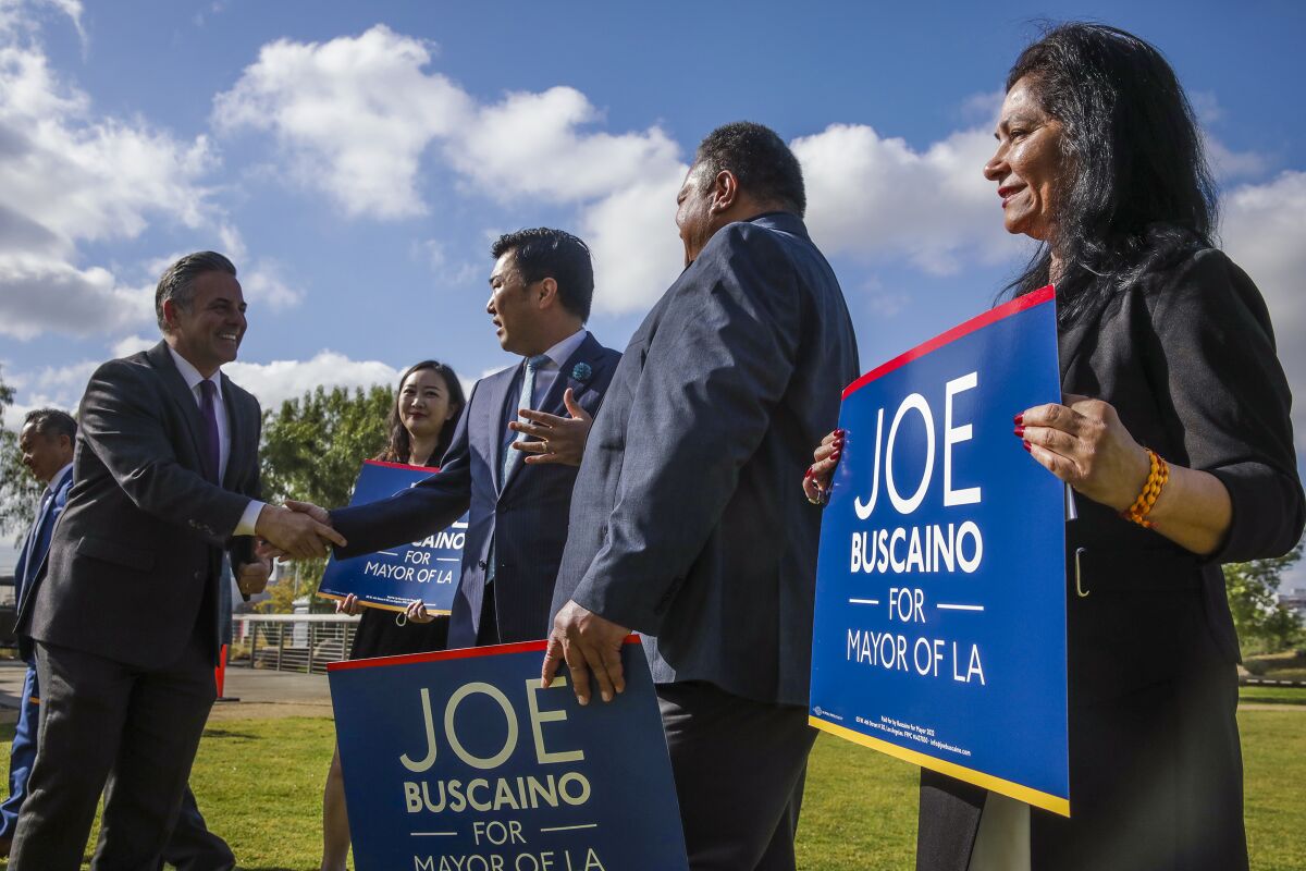 A man in a suit shakes hands with another man next to people holding signs