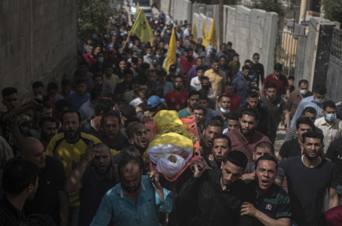 Mourners carry a body wrapped in white and yellow amid a throng of people 