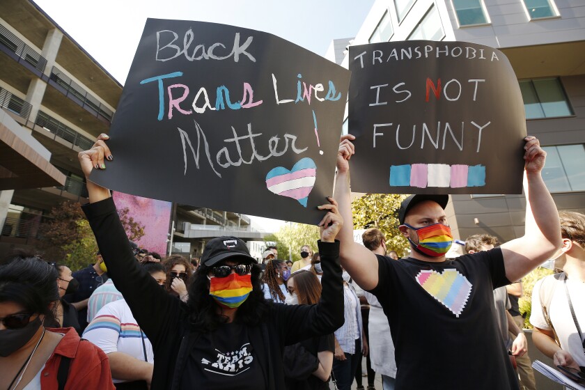 Protesters hold signs that say, "Black trans lives matter," and "Transphobia is not funny."