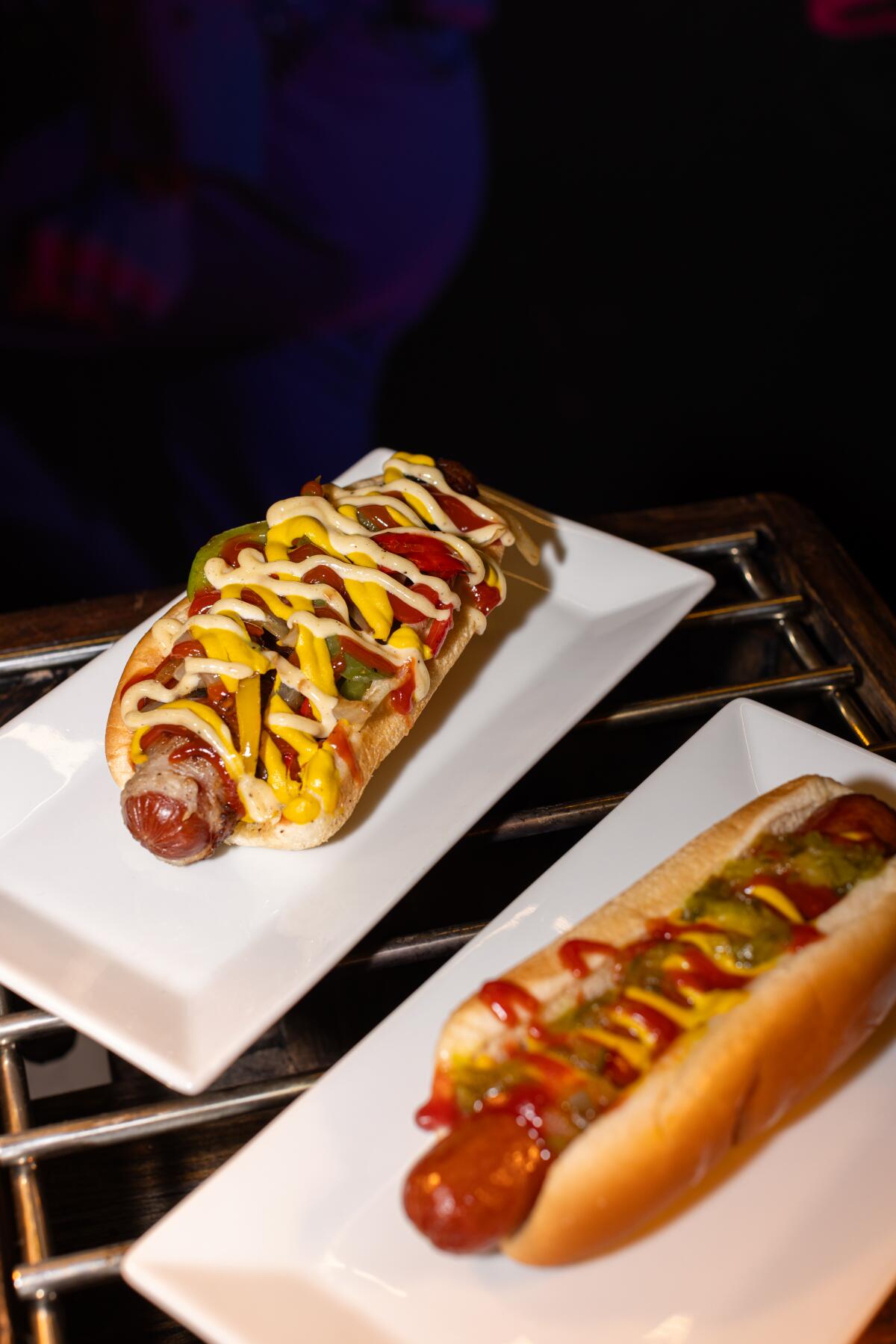 Two hot dogs in buns, side by side, laden with toppings