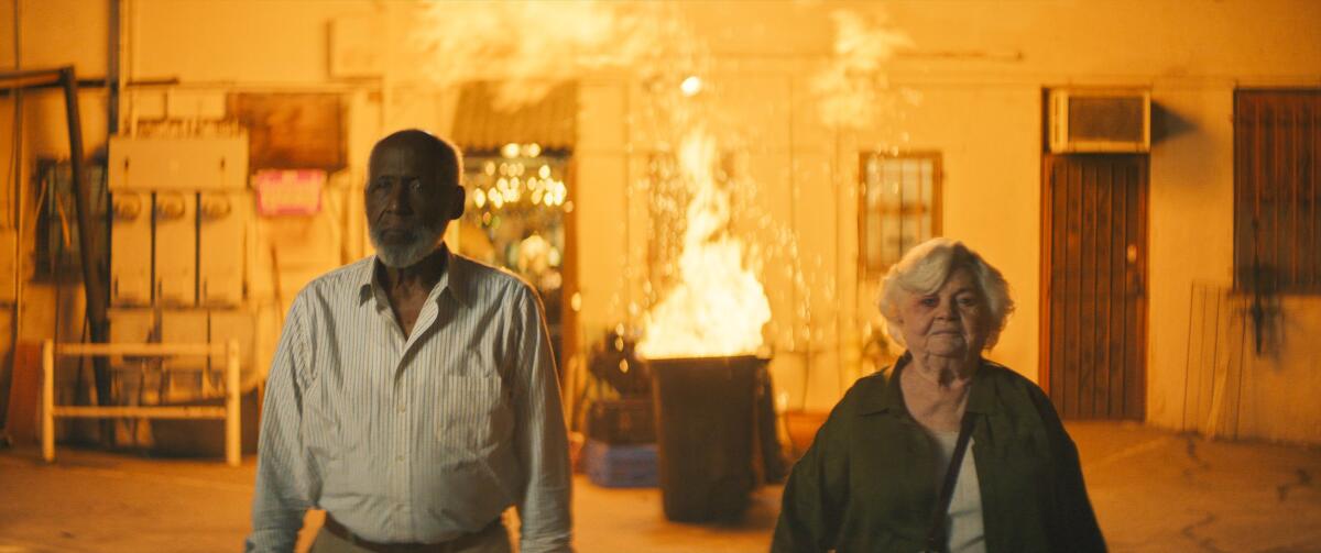 A man and a woman calmly leave a burning room.