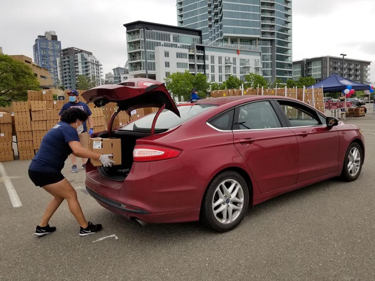 USO volunteer Brigette Jimenez places a box of produce in the back of a vehicle on Saturday. The USO had a drive-through food distribution event for current members of the military and their families near Petco Park as part of Armed Forces Day.