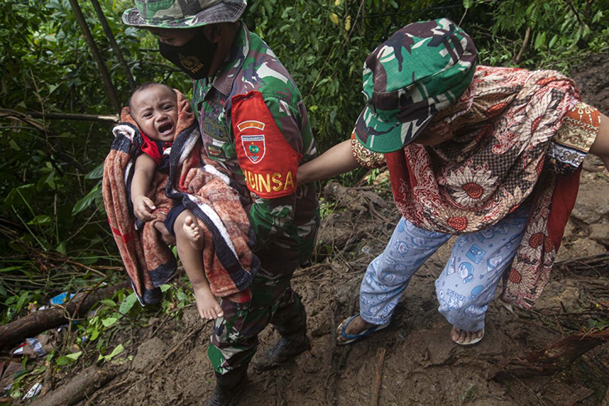 An Indonesian soldier carries a woman's baby as they make their way through an area affected by a landslide.