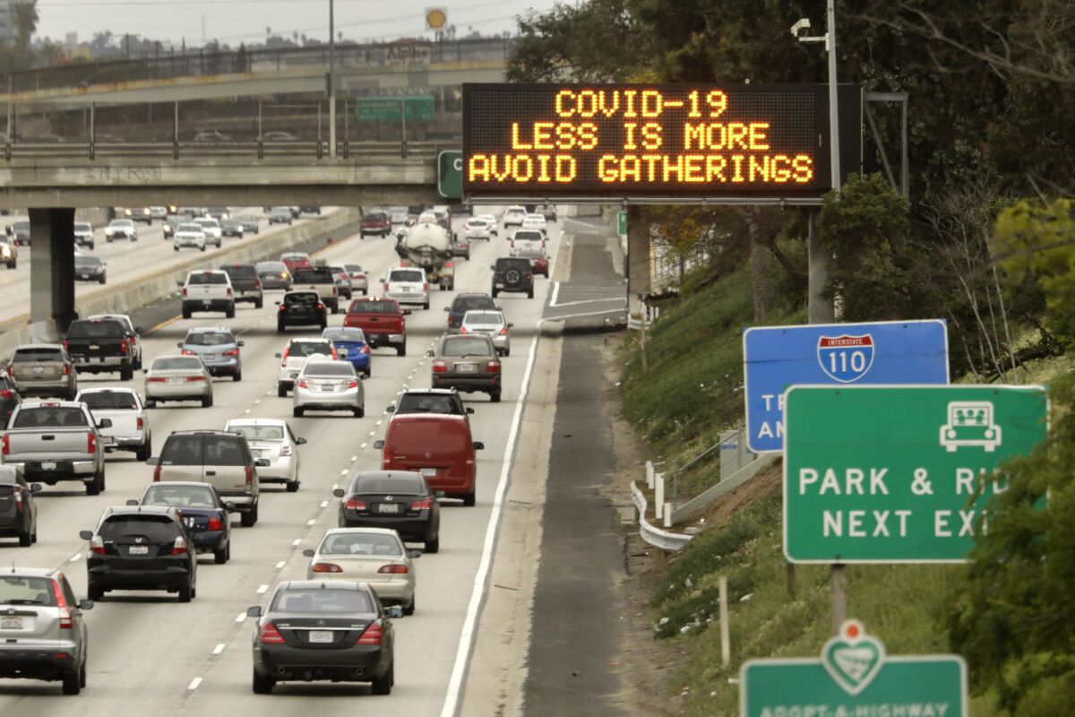 An L.A. freeway sign displays the message: "COVID-19 / LESS IS MORE / AVOID GATHERINGS"