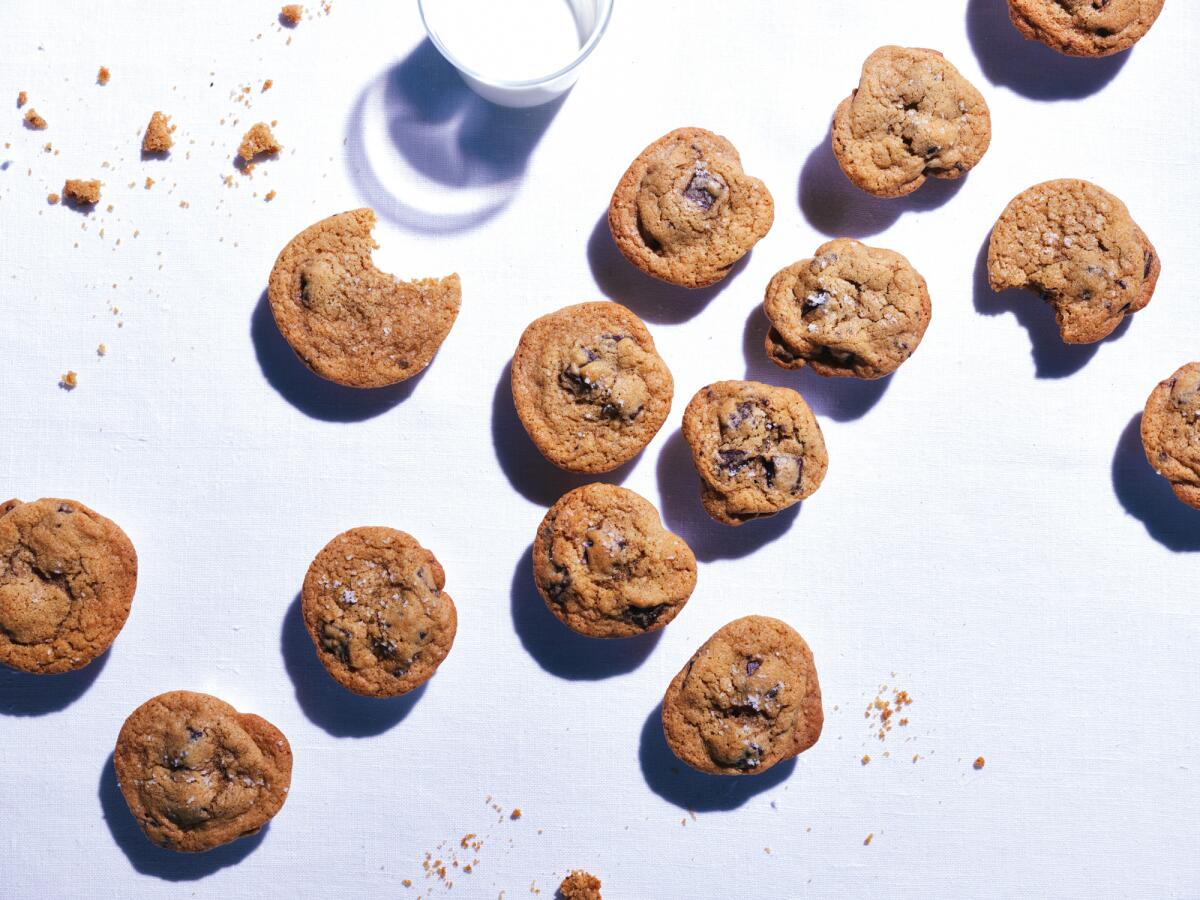 Chocolate chip cookies and a glass of milk sit on a tablecloth.