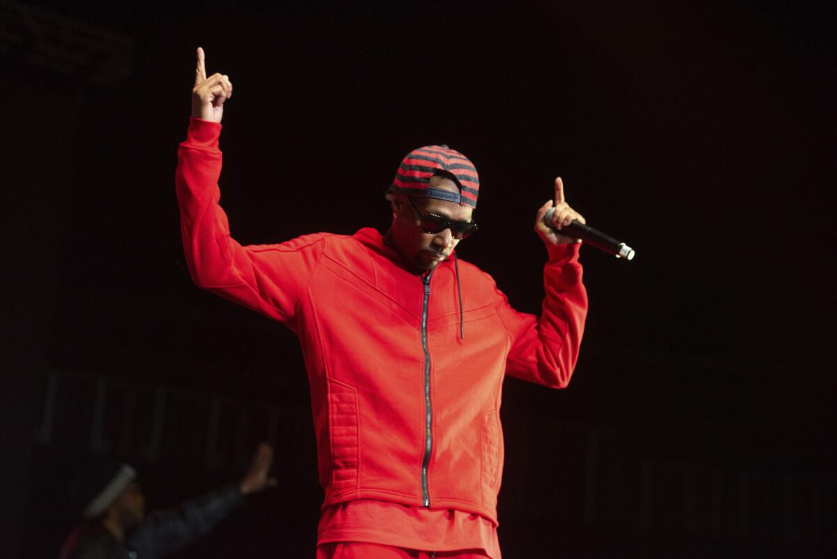 Krayzie Bone wears all red as he performs onstage, holding a mic and pointing to the sky. 