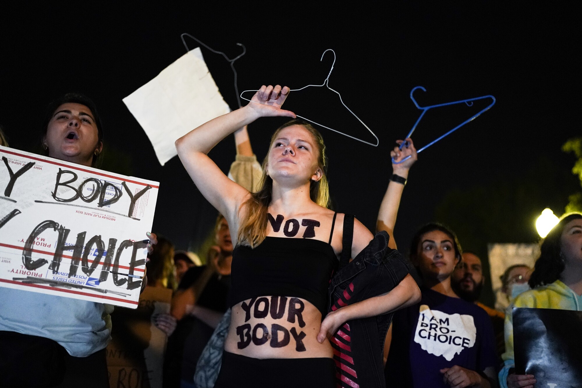 A protester with "Not your body" painted on her body holds up clothes hangers with other protesters