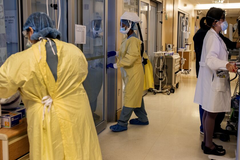 COLTON, CA - JULY 8, 2020: An ICU nurse, middle, wearing a CAPR (Controlled Air Purifying Respirator) enters a negative pressure room to treat a COVID-19 patient at Arrowhead Regional Medical Center on July 8, 2020 in Colton, California. This ICU has only 2 more beds available for Covid patients, but has the capacity to expand to more beds if needed.(Gina Ferazzi / Los Angeles Times)
