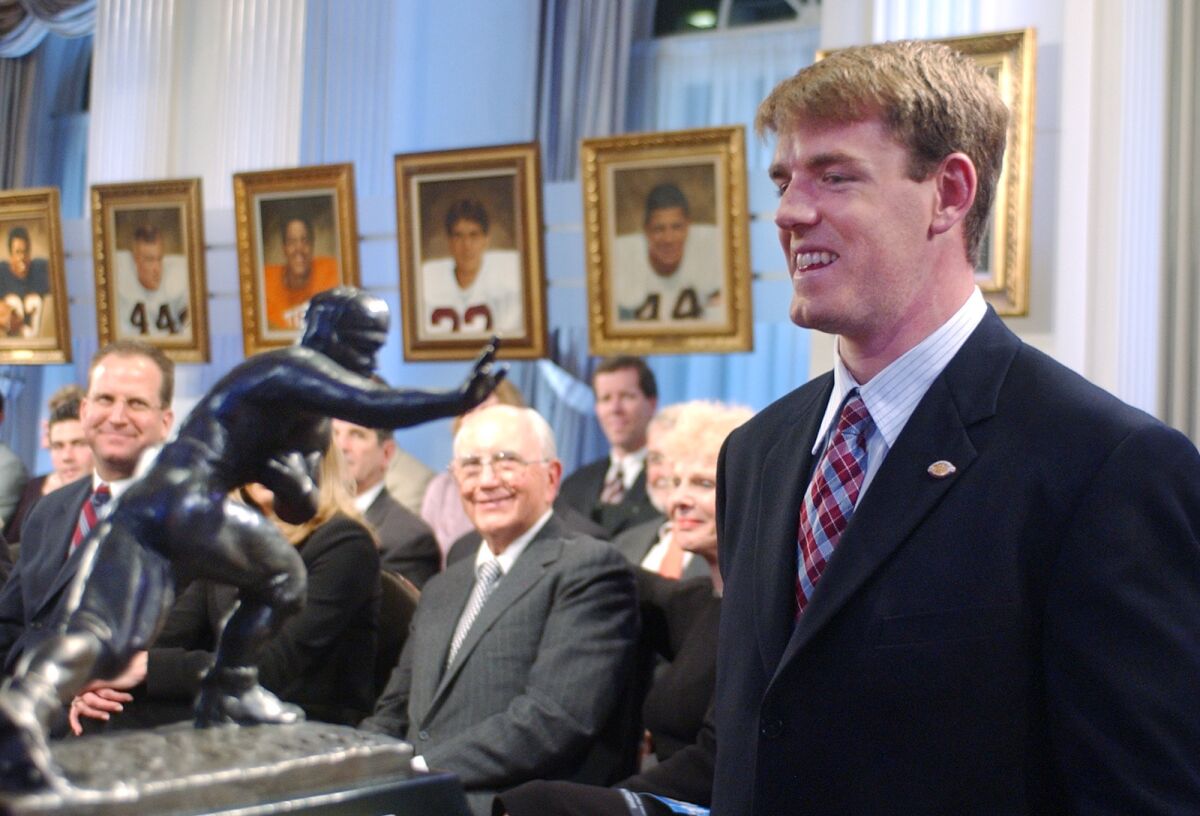 FILE - USC quarterback Carson Palmer, right, smiles at the Heisman Trophy after being named the 2002 Heisman Trophy winner at The Yale Club in New York, in this Dec. 14, 2002, file photo. Heisman Trophy winner Carson Palmer and former Oklahoma coach Bob Stoops are among the 13 former players and coaches who make up the latest College Football Hall of Fame class. The National Football Foundation announced the newly elected hall of famers Monday, Jan. 11, 2021. This class will be inducted in December. (AP Photo/Suzanne Plunkett, File)