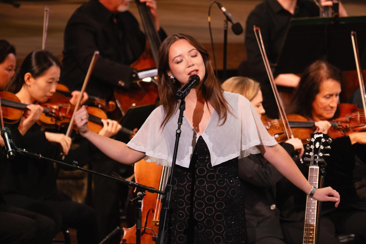 A woman singing into a microphone with an orchestra behind her.