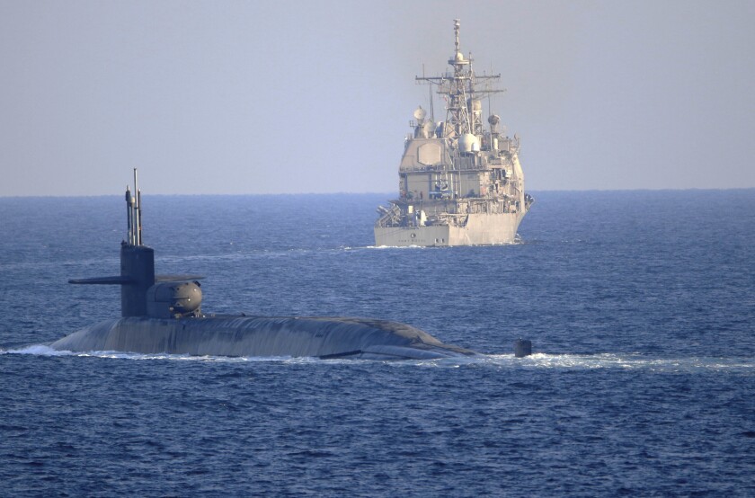 A submarine is seen in the water near a warship.