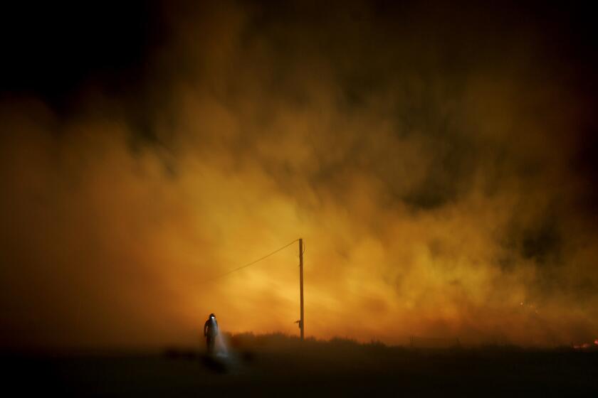 A Chula Vista firefighter walks away from the Harris fire in San Diego County in October. Scientists worry that native coastal sage and chaparral may be replaced by invasive grasses in areas that burned in 2003 and again last year.