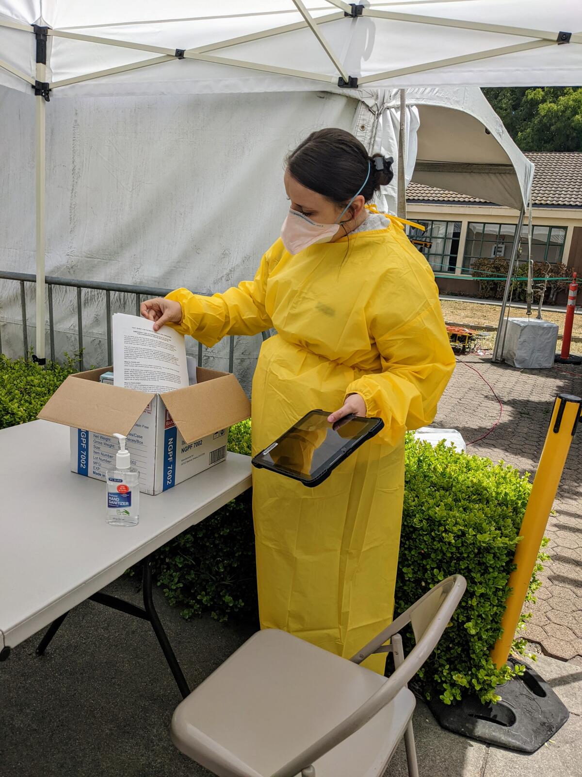 A nurse, standing, goes through a box of paperwork at an outdoor “test-to-treat” site.