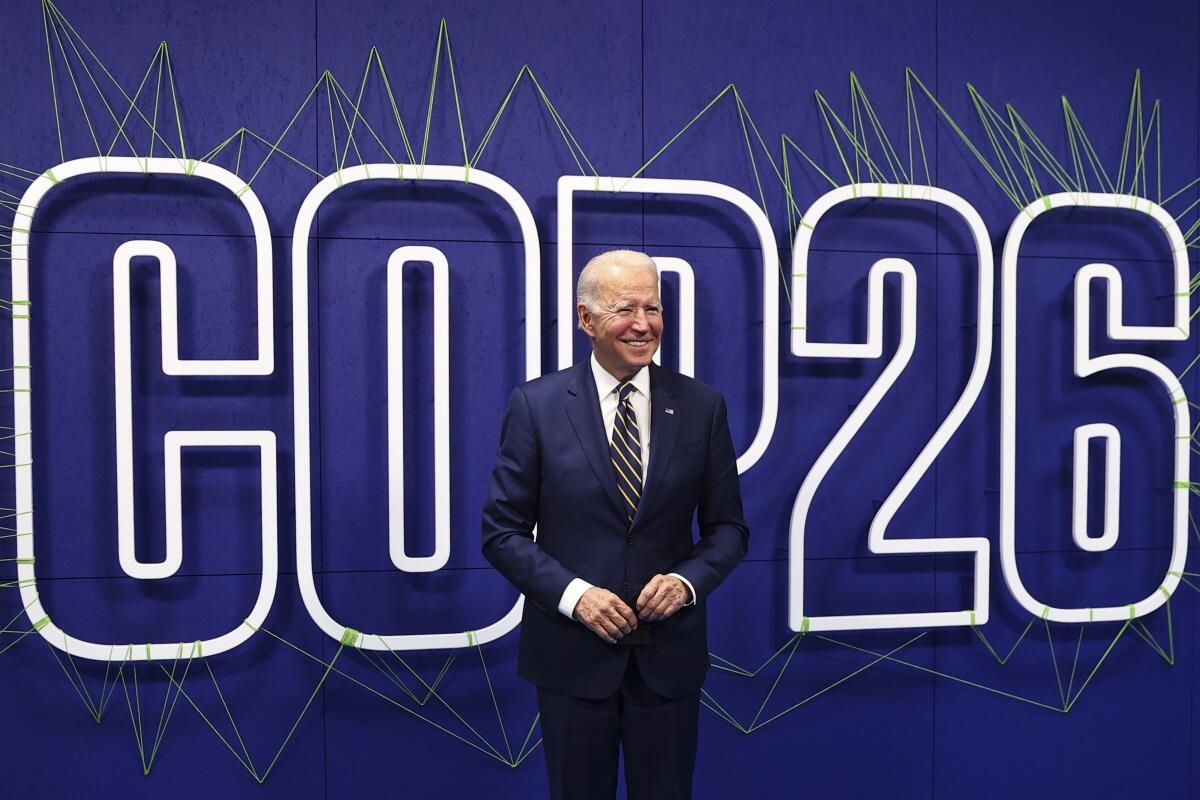 President Biden stands in front of a sign that says COP26.