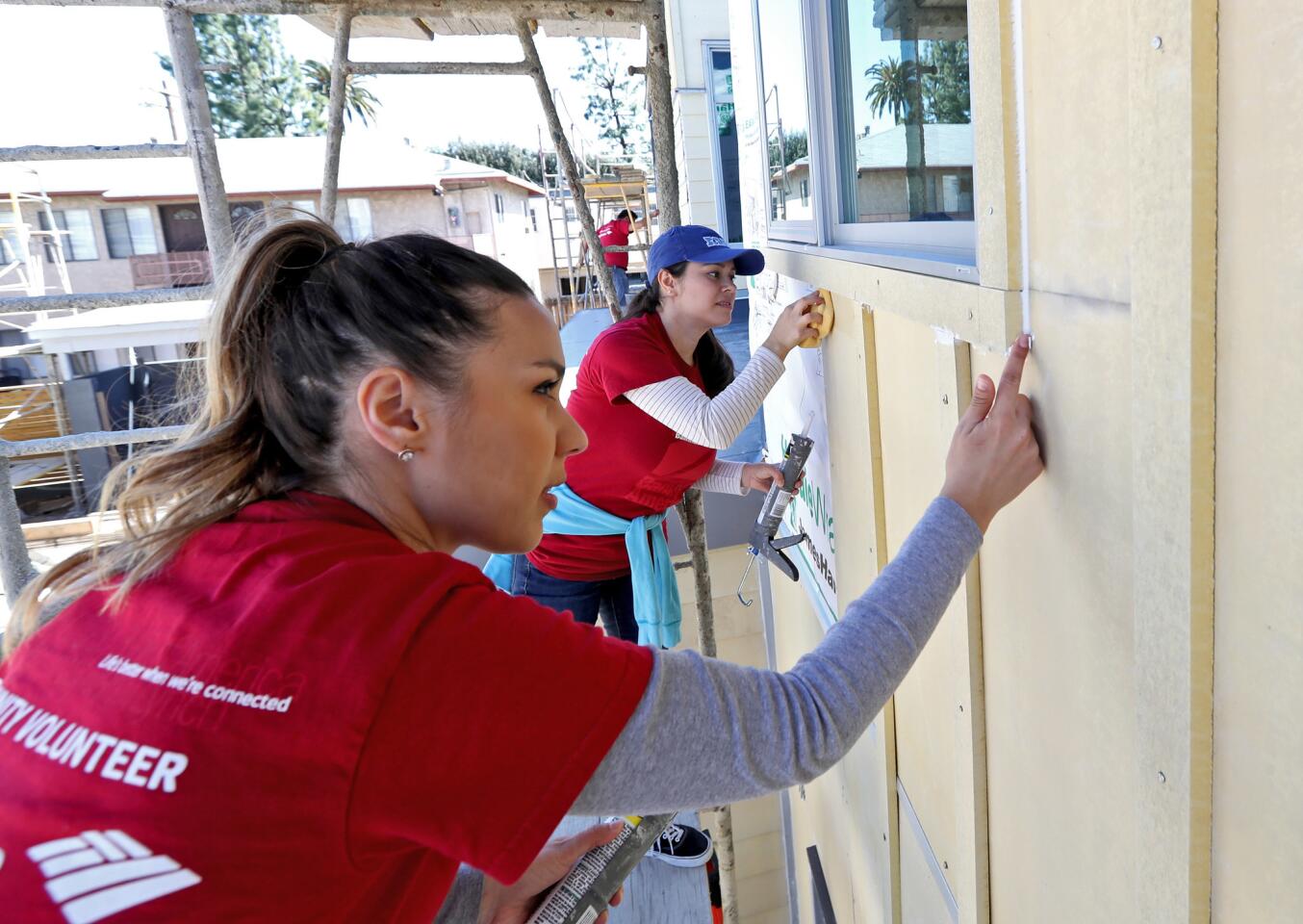 Bank of America employees Yasmin Semerdjian, left, and Yesenia De Leon, right, caulk around windows on a six-home complex being built by the San Gabriel chapter of Habitat for Humanity, on the 700 block of Lomita Ave., in Glendale on Saturday, March 16, 2019.