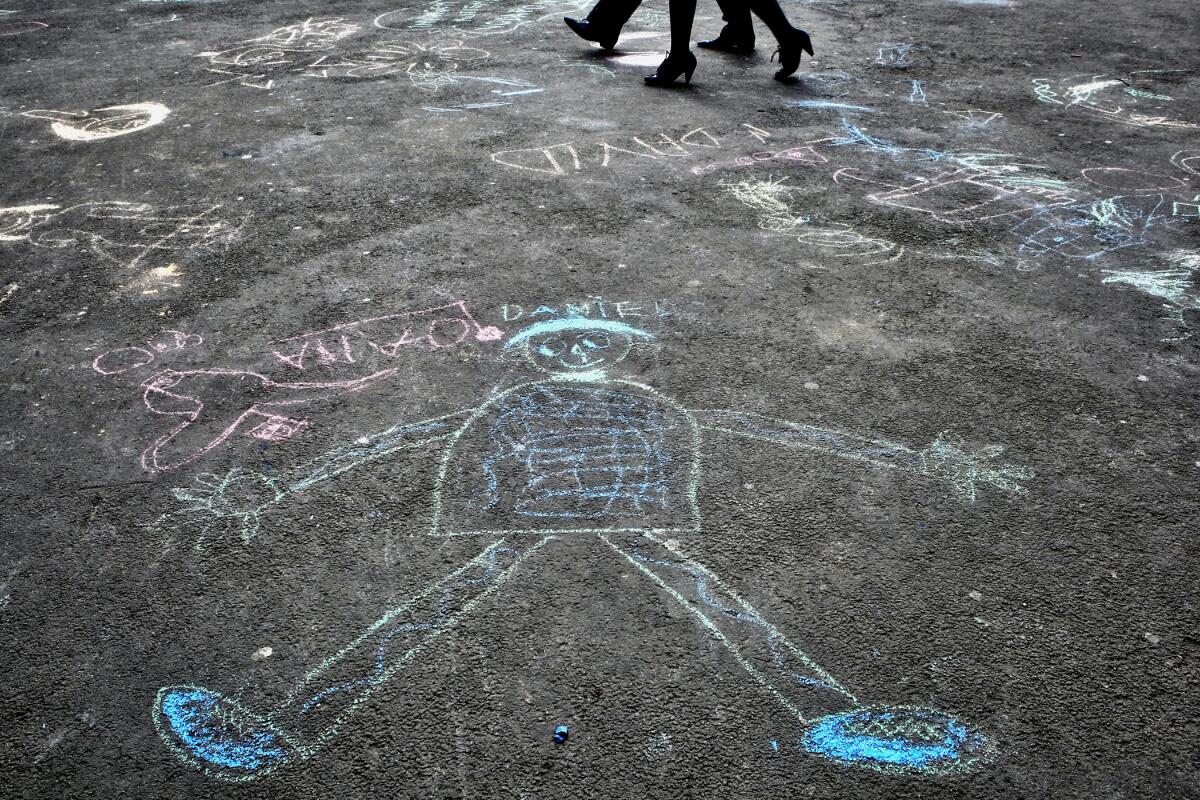 Pedestrians walk past children's chalk drawings on a street