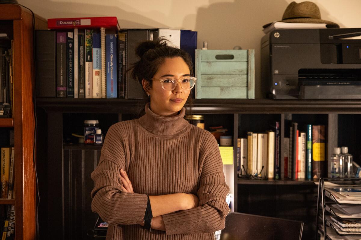 A woman in a brown sweater and wearing glasses poses for a photo in her home office