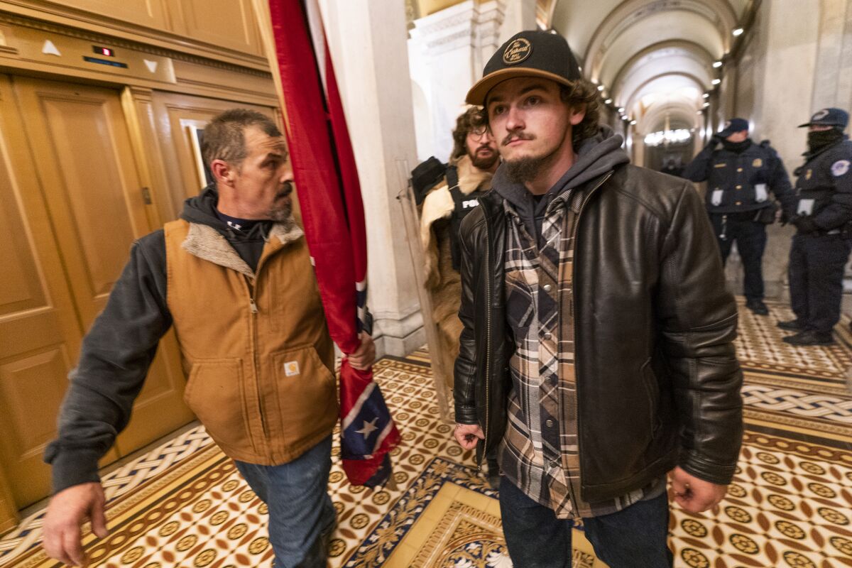 FILE - Insurrectionists loyal to President Donald Trump, including Kevin Seefried, left, walk on a hallway after a confrontation with Capitol Police officers outside the Senate Chamber inside the Capitol, Jan. 6, 2021 in Washington. A federal trial is scheduled to start on Monday, June 13, for Seefried and his son Hunter who have been charged with storming the U.S. Capitol together. (AP Photo/Manuel Balce Ceneta, File)