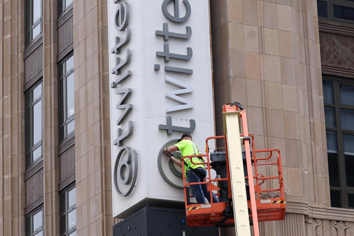 A man in an orange crane pushing a tool against a letter in the Twitter sign on the headquarters of the platform.