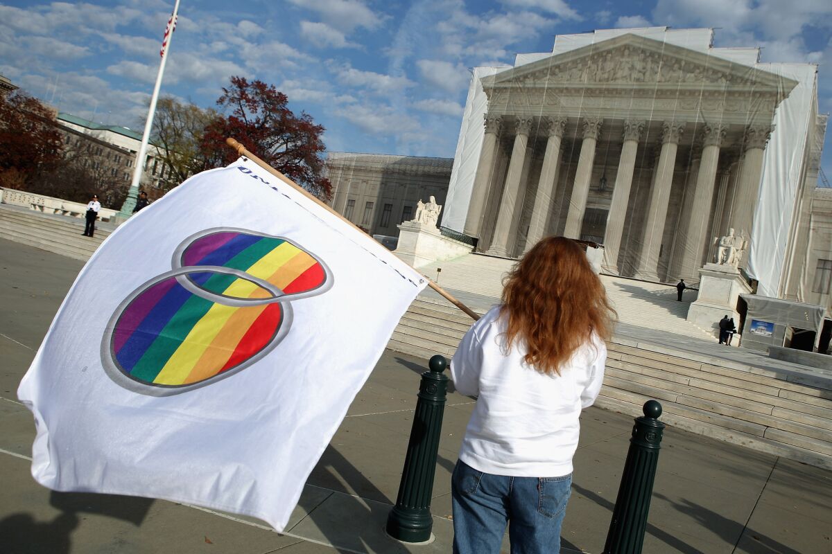 A same-sex marriage proponent holds a gay marriage pride flag while standing in front of the Supreme Court.