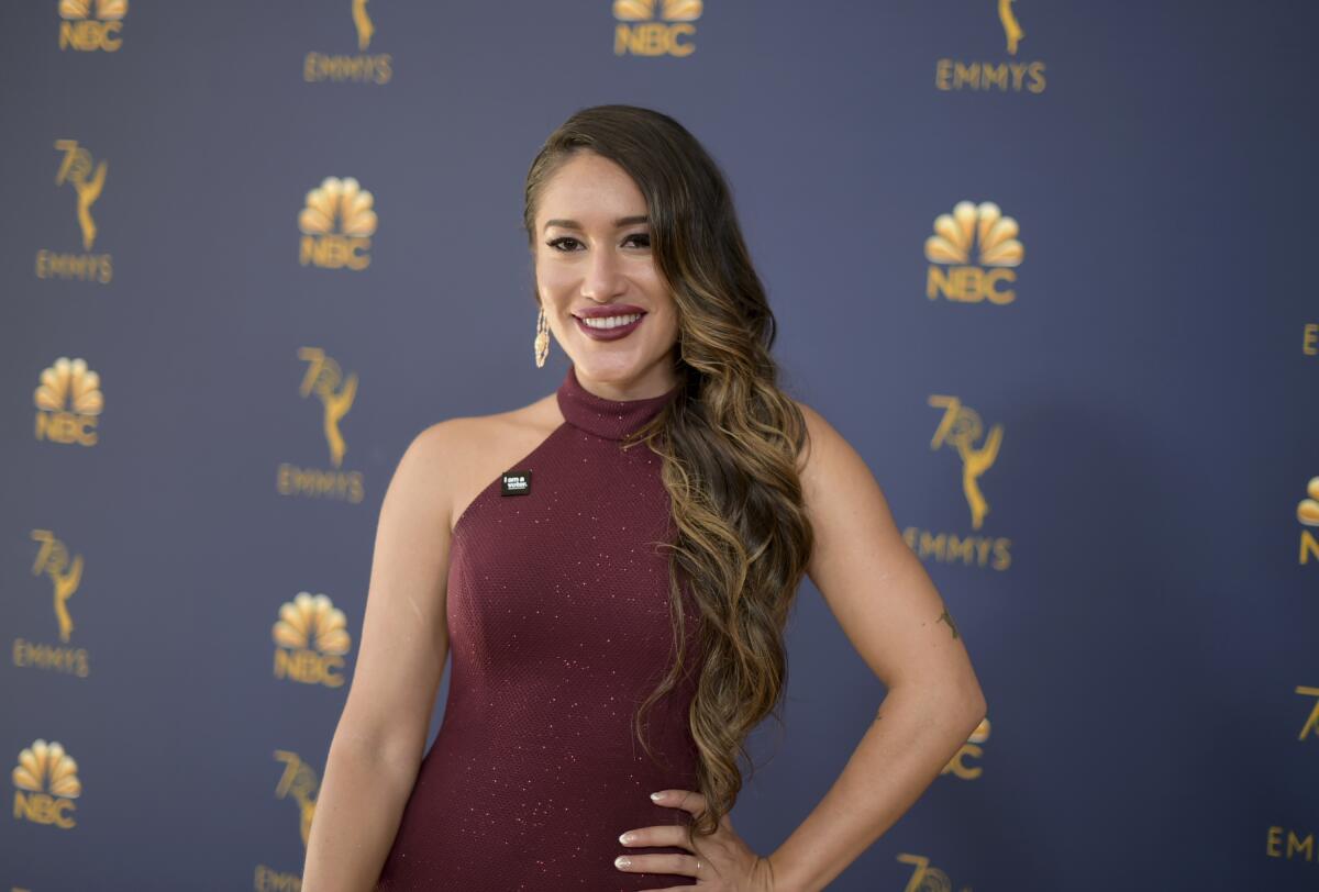 A woman with long, brown hair in a burgundy dress poses smiles at a red carpet. 